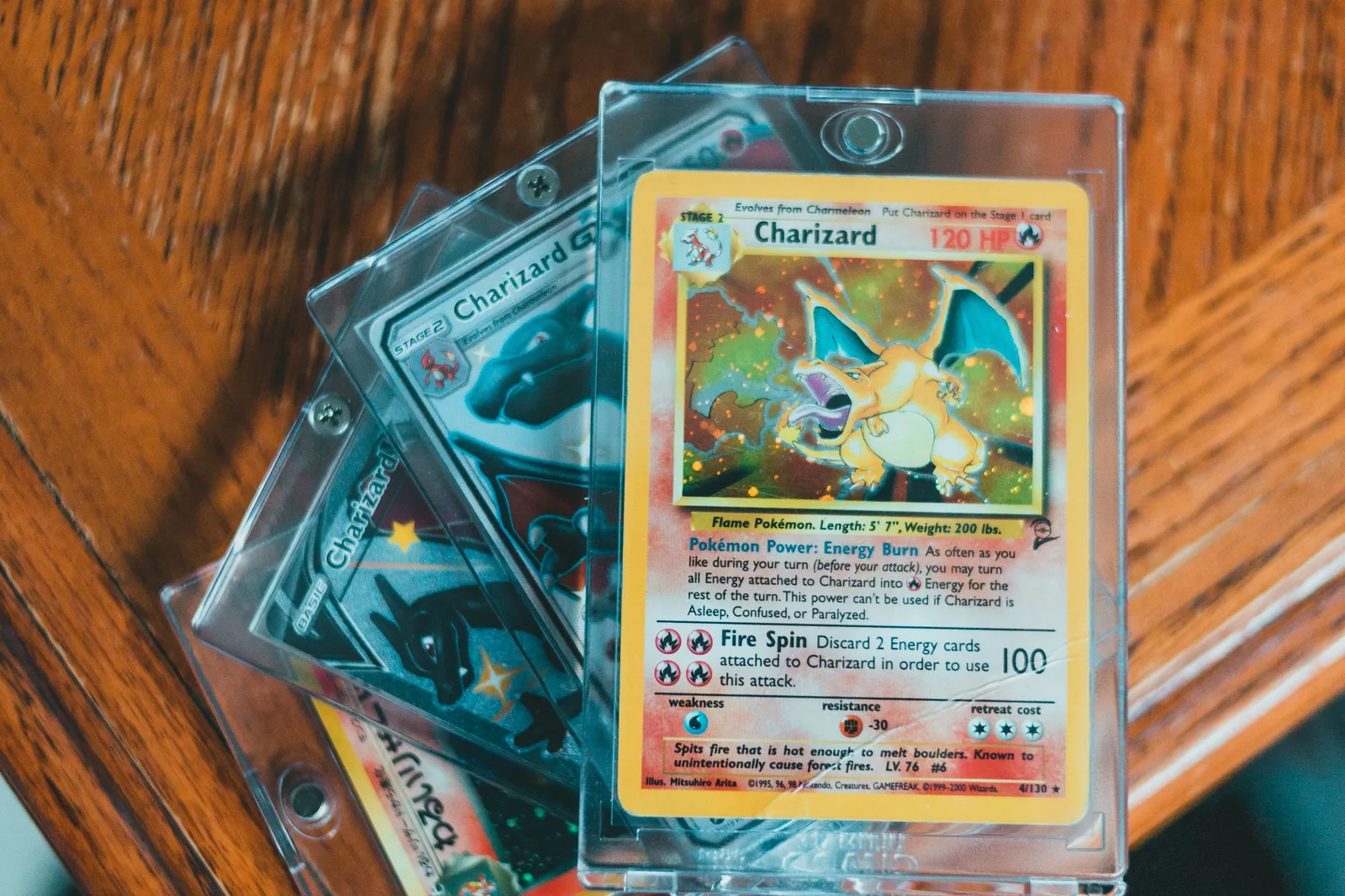 Four ungraded Charizard cards in clear screw down plastic holders stacked on a wooden table, the top one a Charizard numbered 4/130