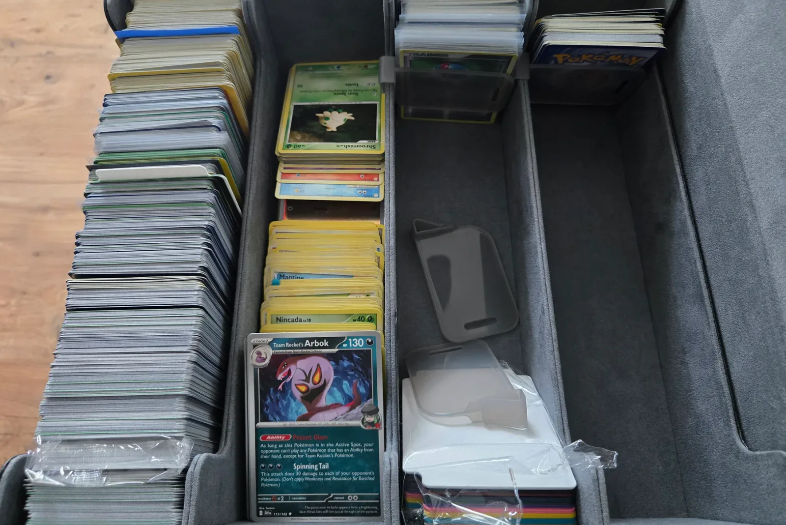 A multi row storage box on a wooden table with a packed row of cards on the left, sorted stacks in progress in the middle, and toploadered cards at the back right