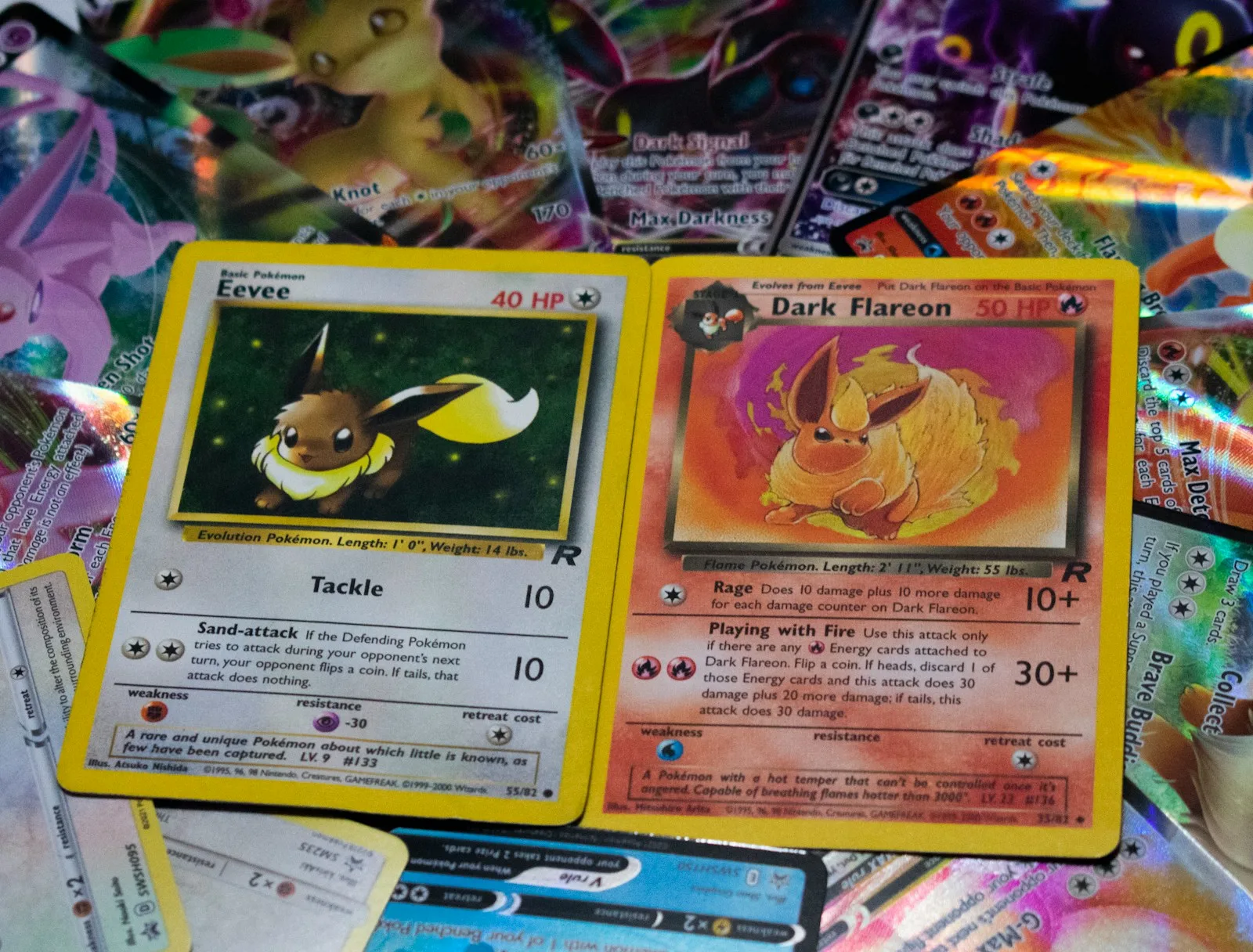 Two older Pokemon cards, an Eevee and a Dark Flareon, lying face up on a dense pile of holofoil cards