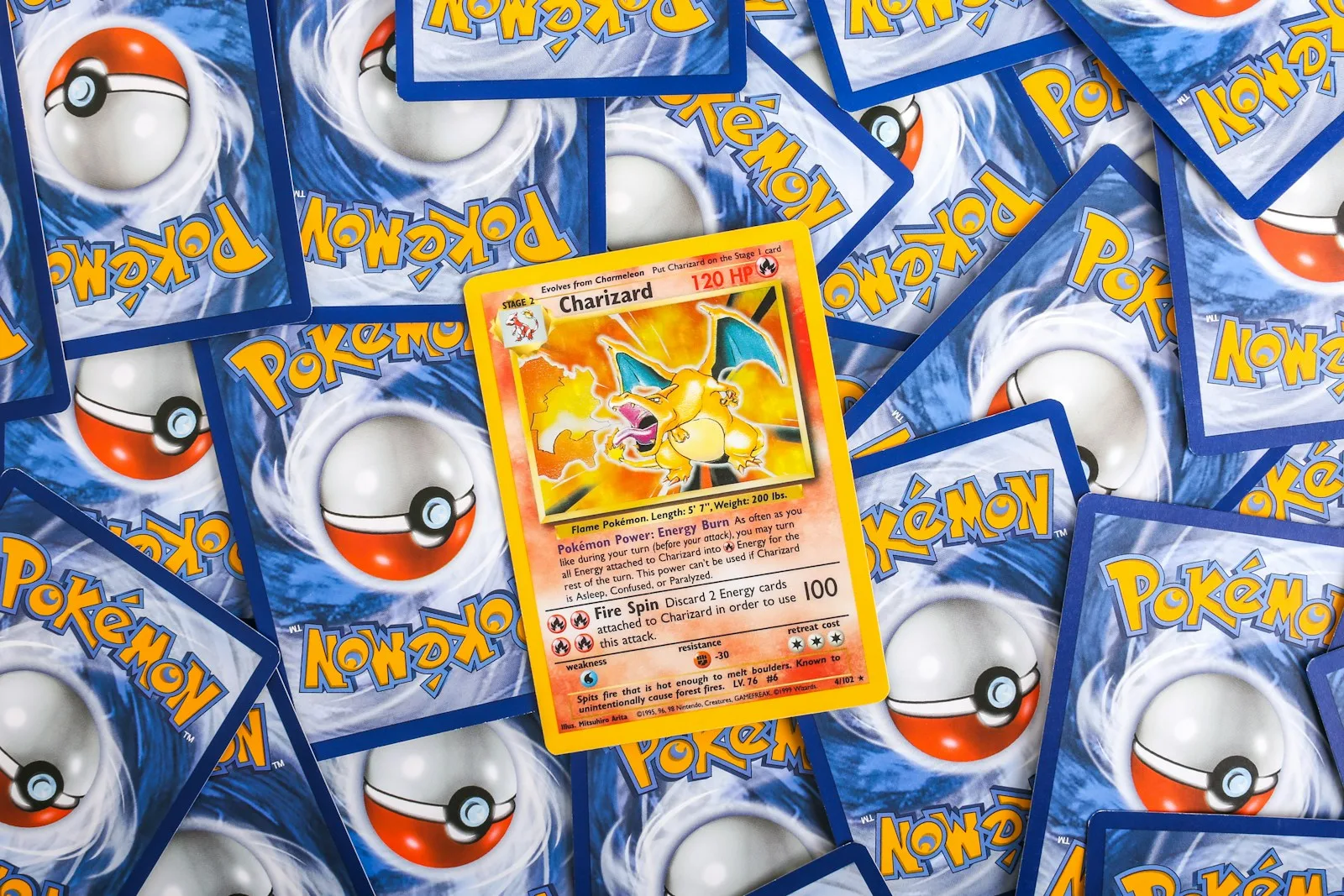 A dense carpet of Pokemon cards lying face down showing their blue Pokeball backs, with one Base Set Charizard lying face up in the middle