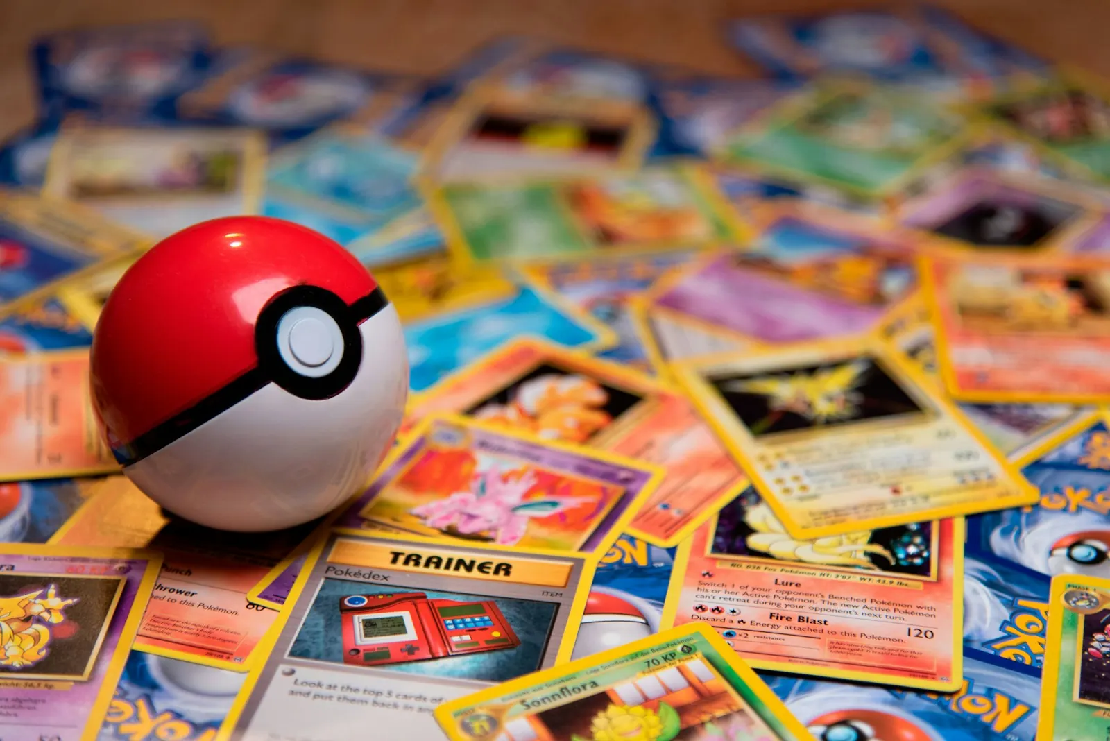A Pokeball toy resting on a scattered pile of Pokemon cards on a table