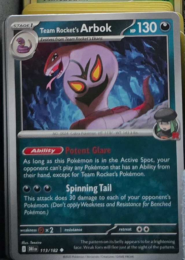 A single Pokemon card standing upright at the front of a packed row of cards inside a storage box, its artwork facing the camera
